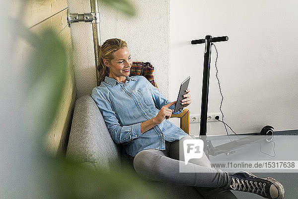 Young woman sitting on couch in a coffe shop  using digital tablet  e-scooter charging in background