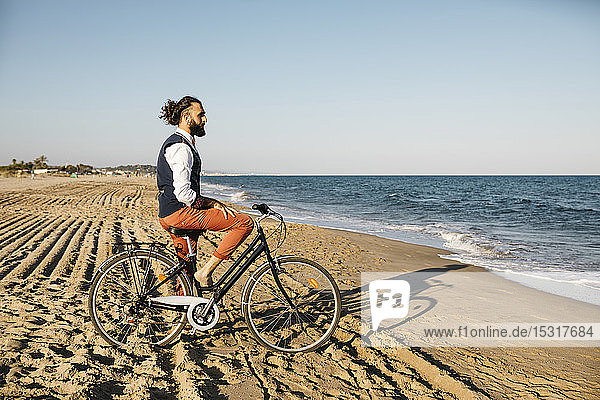 Gut gekleideter Mann mit seinem Fahrrad am Strand