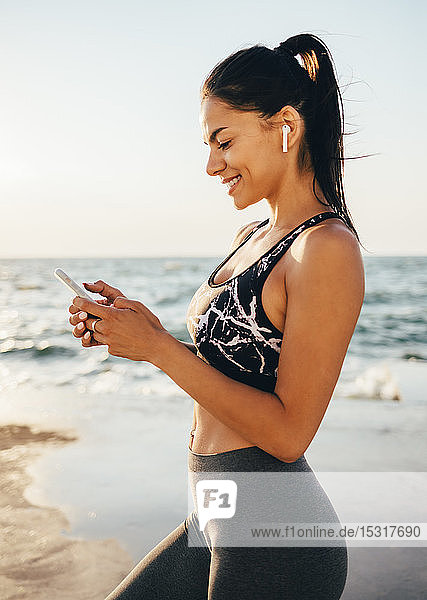 Woman using smartphone and in-ear during workout  sitting on a pier