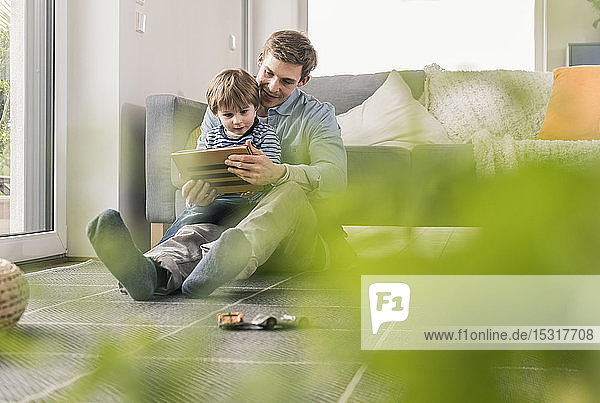 Vater und Sohn sitzen auf dem Boden und benutzen ein digitales Tablett