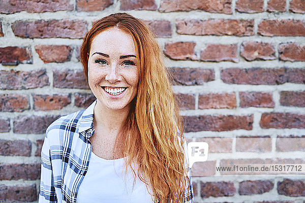 Porträt einer schönen jungen Frau  die vor einer Ziegelmauer vor der Kamera lächelt