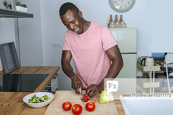 Junger Mann in der Küche schneidet Tomate für einen Salat