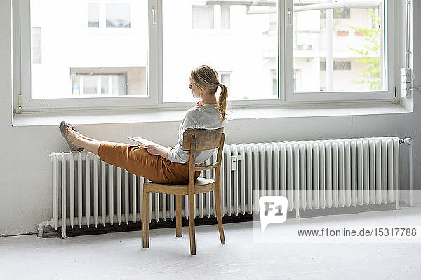 Junge Frau sitzt im Büro auf einem Stuhl am Fenster