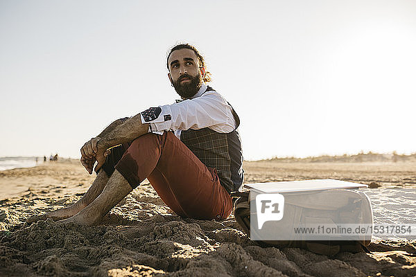 Well dressed man sitting on a beach looking around