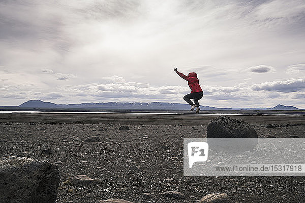 Junge Frau springt von einem Felsen im vulkanischen Hochland von Island