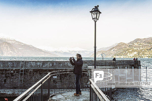 Man using mobile phone taking photos at Lake Como in winter Italy
