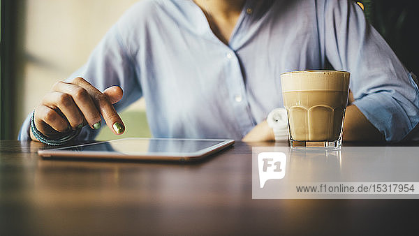 Frau sitzt in einem Café mit einem digitalen Tablet und trinkt einen Kaffee
