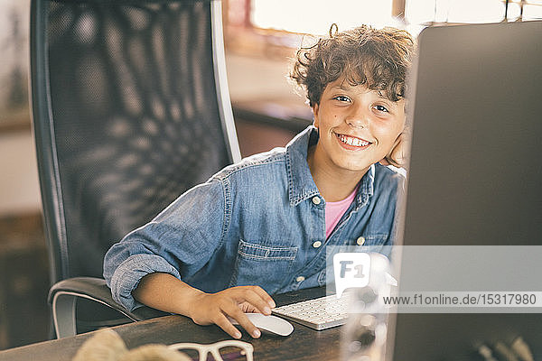 Porträt eines lächelnden Jungen  der zu Hause am Schreibtisch sitzt und seinen PC benutzt