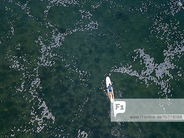 Luftaufnahme einer auf einem Surfbrett liegenden Surferin
