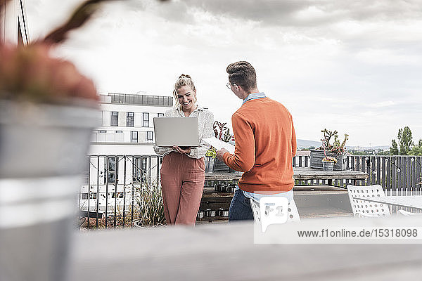 Casual businessman and woman with laptop meeting on roof terrace