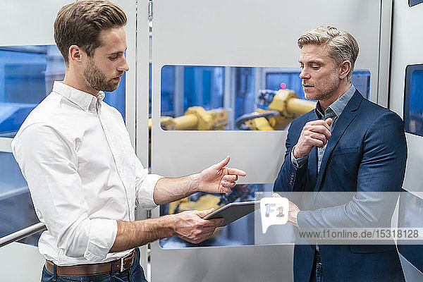 Two businessmen talking at robot in a modern factory