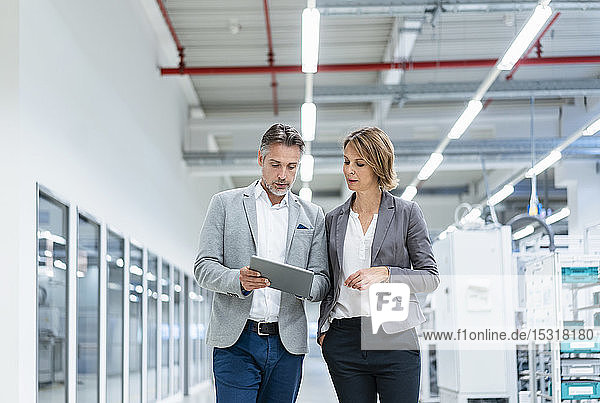 Geschäftsfrau und Geschäftsmann mit Tablette beim Gehen und Sprechen in einer modernen Fabrik