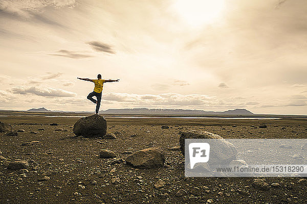 Mature man balancing on one leg on a rock in the volcanic highlands of Iceland