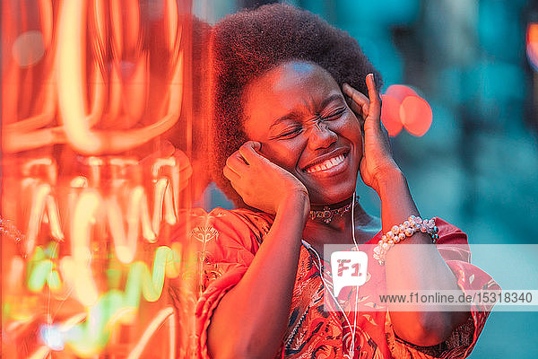 Lächelnde junge Frau mit Kopfhörer neben Neonlicht stehend
