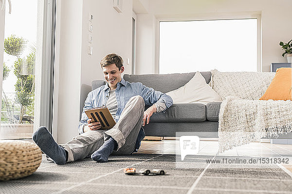Mittelgroßer erwachsener Mann sitzt auf dem Boden und benutzt ein digitales Tablett