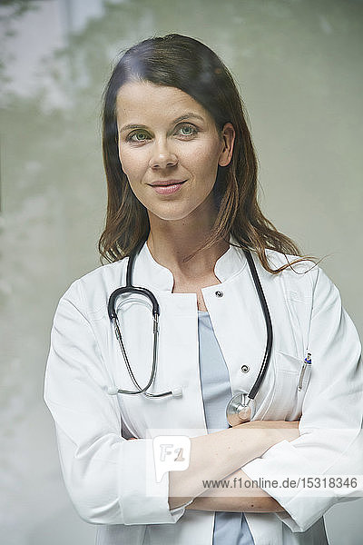 Porträt einer selbstbewussten Ärztin hinter einer Fensterscheibe