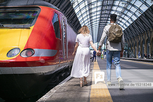 Rückenansicht eines jungen Paares  das Hand in Hand auf dem Bahnsteig geht  London  UK