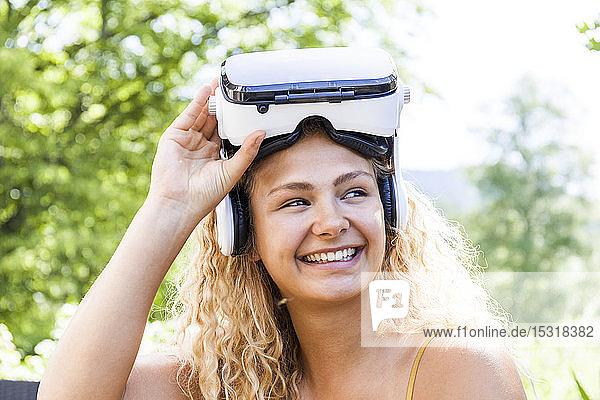 Junge blonde Frau  die im Freien eine Virtual-Reality-Brille trägt und zur Seite schaut