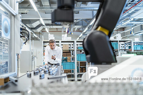 Businessman in a modern factory hall looking at robot