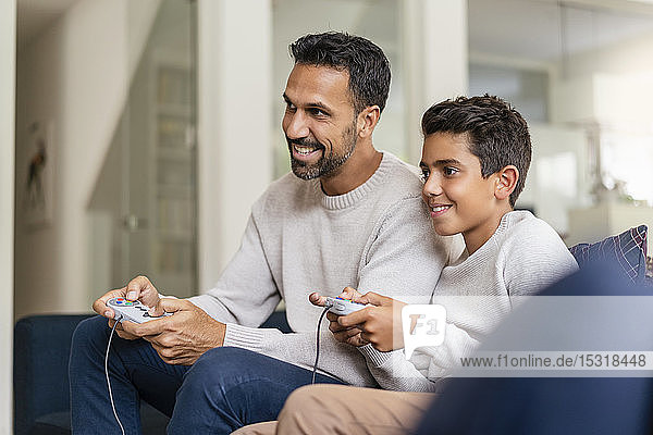 Happy father and son playing video game on couch in living room