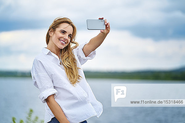 Glückliche Frau  die mit einem Smartphone am Seeufer Selbsthilfe betreibt