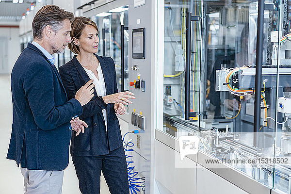 Businessman and businesswoman looking at a machine in a modern factory hall