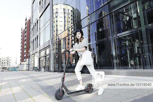 Frau mit E-Scooter und Helm  im Hintergrund moderne Bürogebäude