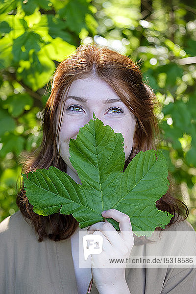 Weibliche Teenagerin in einem Wald  die ein Blatt vor den Mund hält