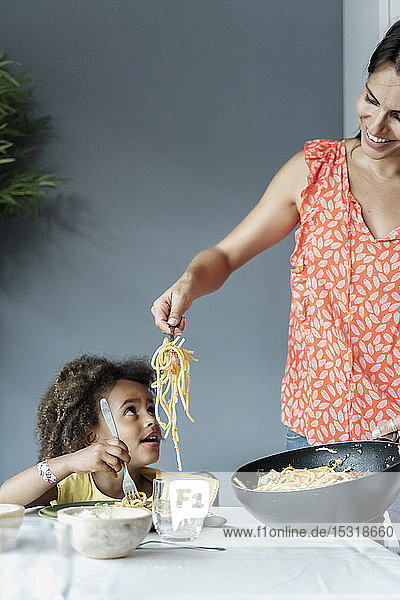 Mother serving pasta meal for daughter sitting at dining table