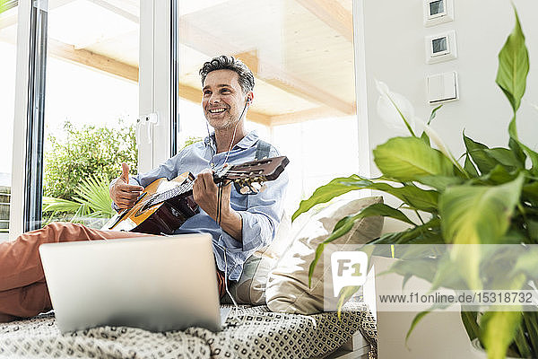 Mature man practising on the guitar using laptop and earphones