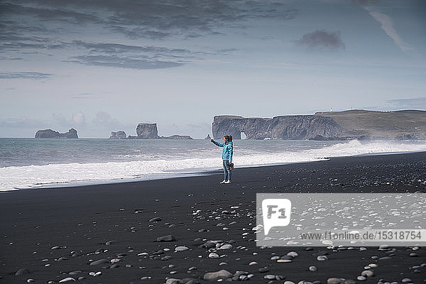 Junge Frau beim Fotografieren an einem Lavastrand in Island
