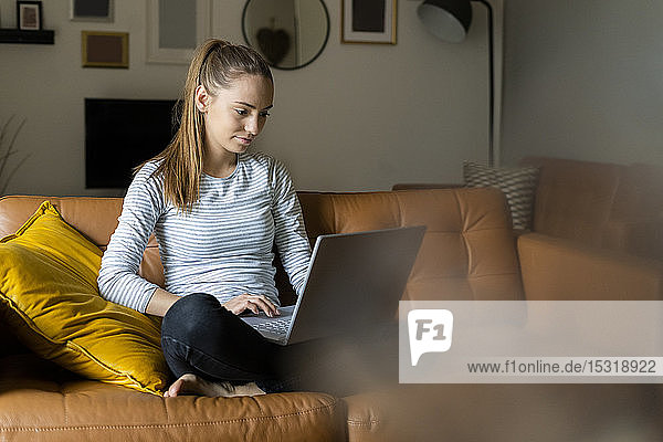 Junge Frau benutzt Laptop zu Hause auf der Couch