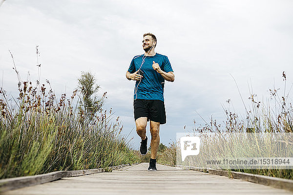 Jogger with earphones running on a wooden walkway