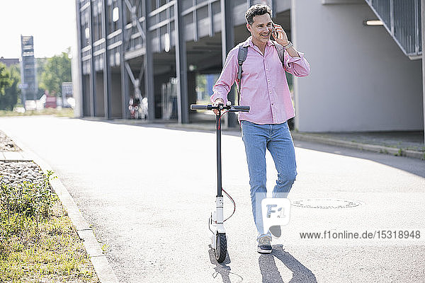 Businessman using smartphone  pushing his E-Scooter