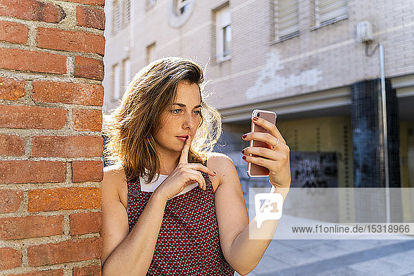 Junge Frau lehnt an Ziegelsteinmauer und nimmt ein Selfie