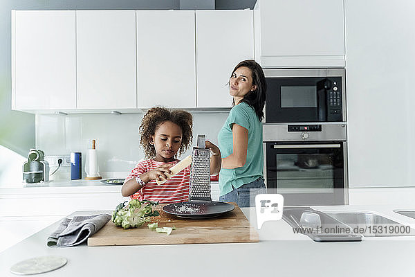 Girl cooking with mother in kitchen grating cheese
