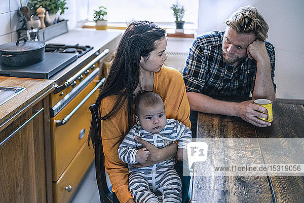 Ernste Familie mit einem Baby  das zu Hause am Küchentisch sitzt