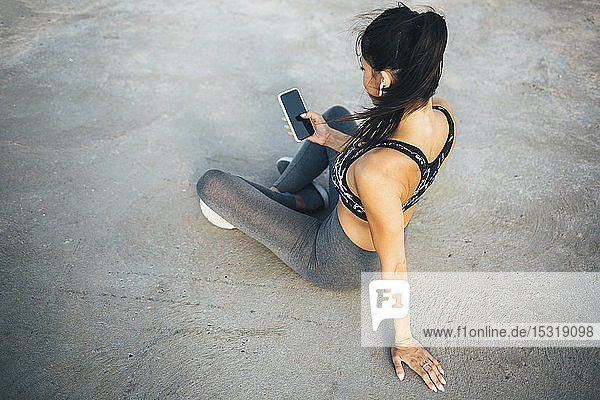Woman using smartphone and in-ear during workout  sitting on a pier