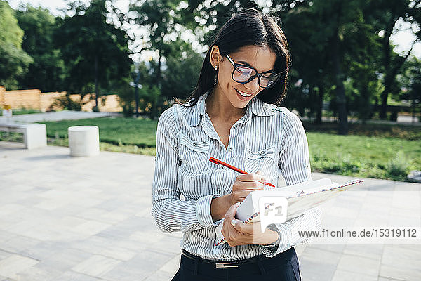 Lächelnde junge Geschäftsfrau macht Notizen im Freien