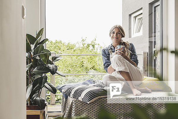 Porträt einer Frau  die zu Hause am Fenster sitzt und eine Kaffeepause macht