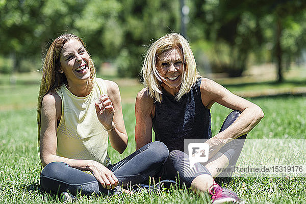 Glückliche sportliche reife Frau und ihre Tochter sitzen auf einer Wiese in einem Park