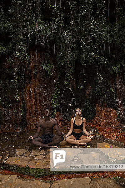 Paar beim Meditieren an einem Wasserfall