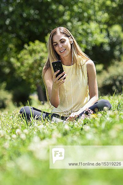 Frau  die ihr Smartphone benutzt und sich nach dem Sport im Gras eines Parks ausruht