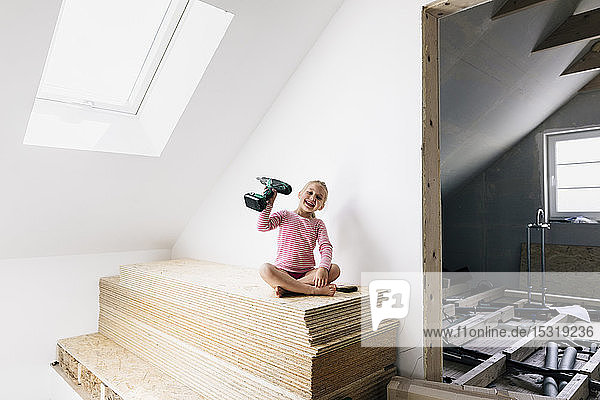 Porträt eines glücklichen Mädchens mit einer elektrischen Bohrmaschine in einem zu renovierenden Haus