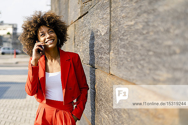 Porträt einer lächelnden jungen Frau am Telefon in einem modischen roten Hosenanzug