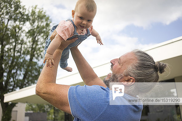 Happy mature man lifting up baby girl in garden of his house