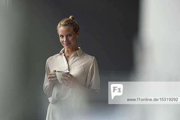 Porträt einer lächelnden jungen Geschäftsfrau mit Tasse Kaffee