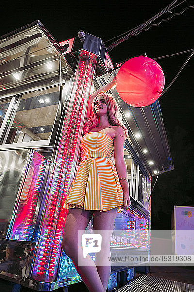 Glückliche junge Frau mit einem Ballon auf einem nächtlichen Rummelplatz