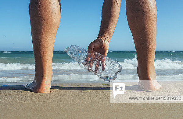 Mann steht am Meeresufer und hebt eine leere Plastikflasche auf  Nahaufnahme