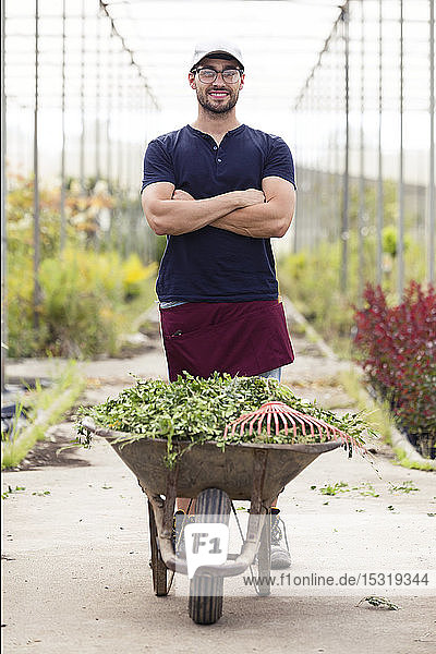 Portrait of young man with wheelbarrow in the greenhouse